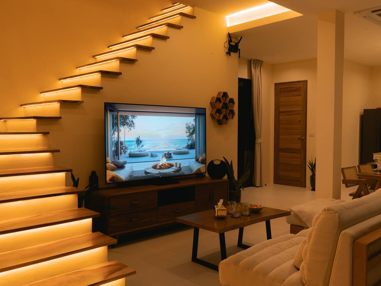 Open-plan living at night with floating stairs and 75 inch TV